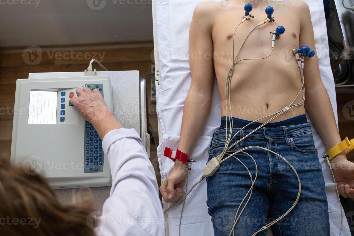A female doctor performs an ECG on a young man in a hospital room, carefully monitoring his heart health during a routine checkup. photo