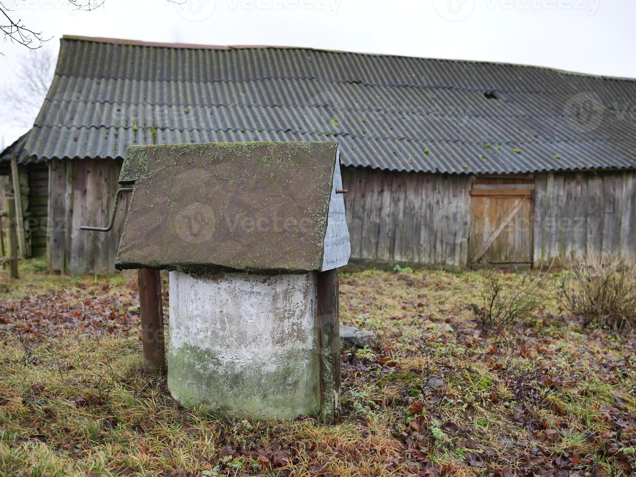 A charming, rustic well stands prominently in front of an old, weathered barn amidst a serene countryside setting photo