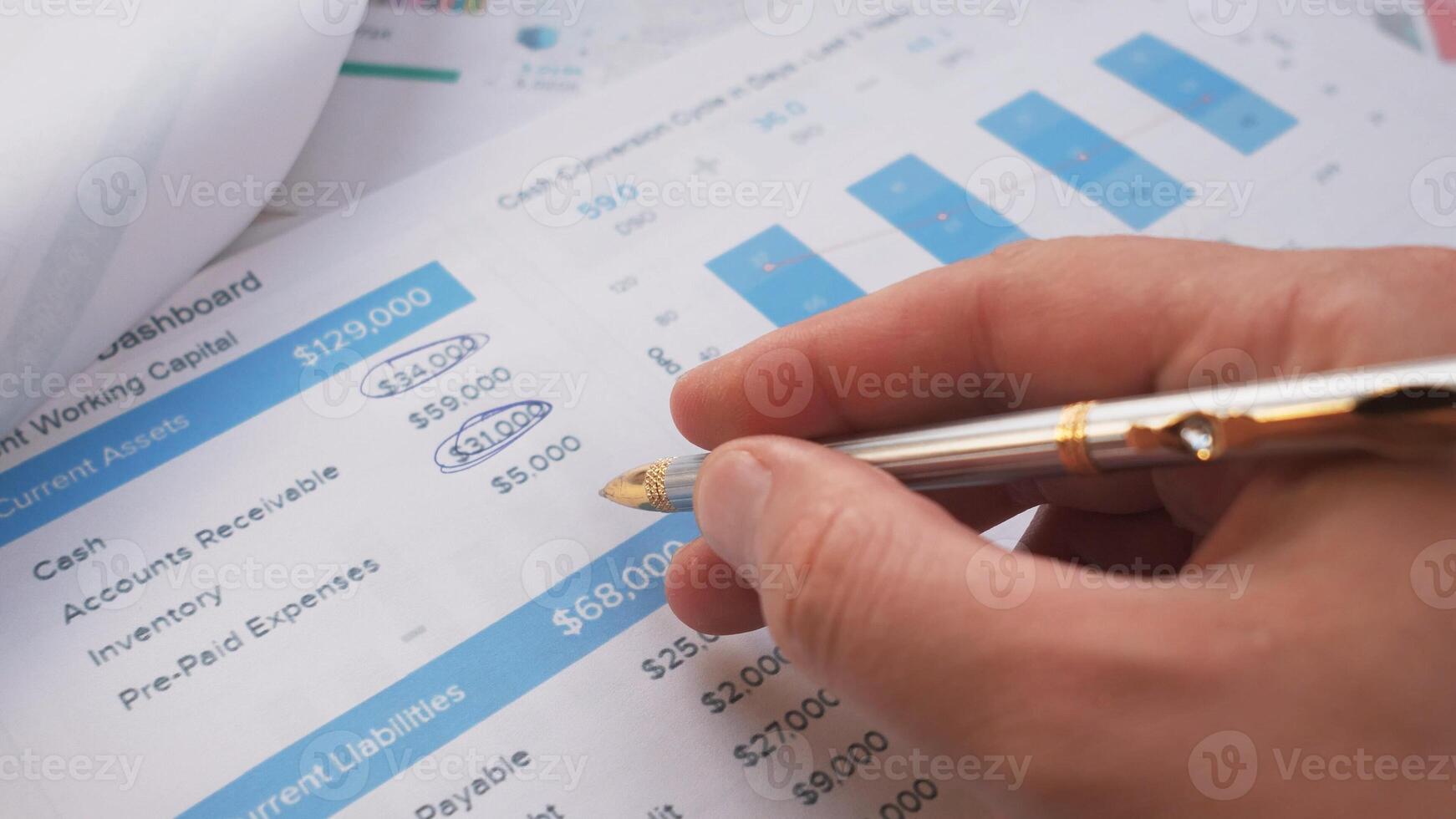 A hand holds a pen over financial documents, emphasizing crucial detailed analysis of important data photo