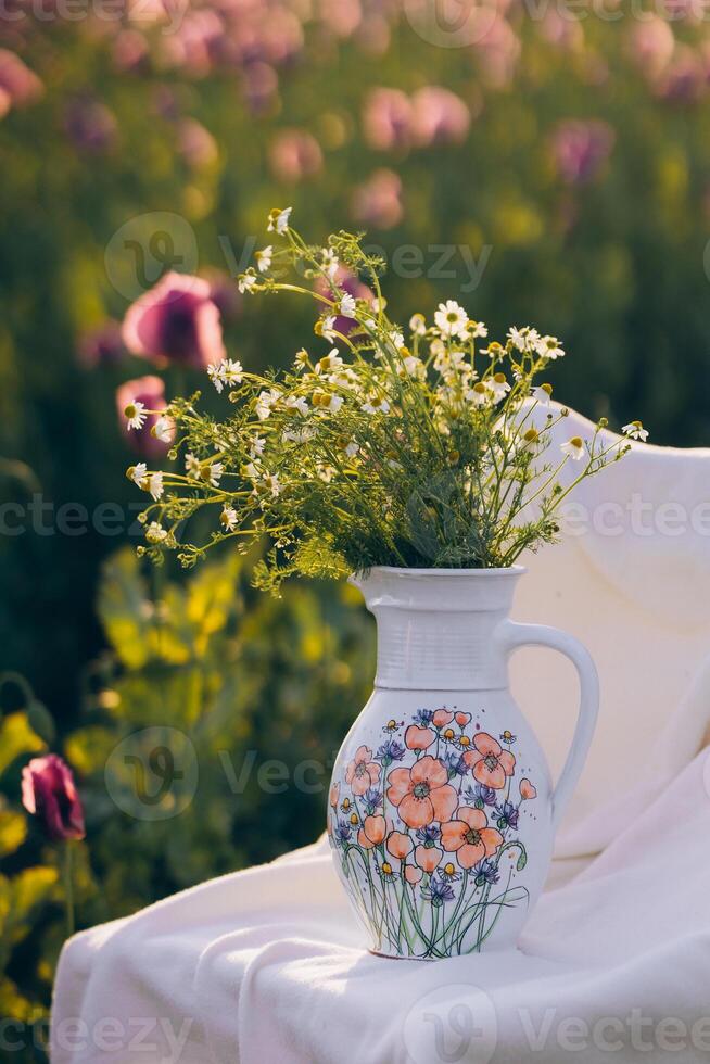 Still life with flowers and a chair in a field of poppies at sunset photo