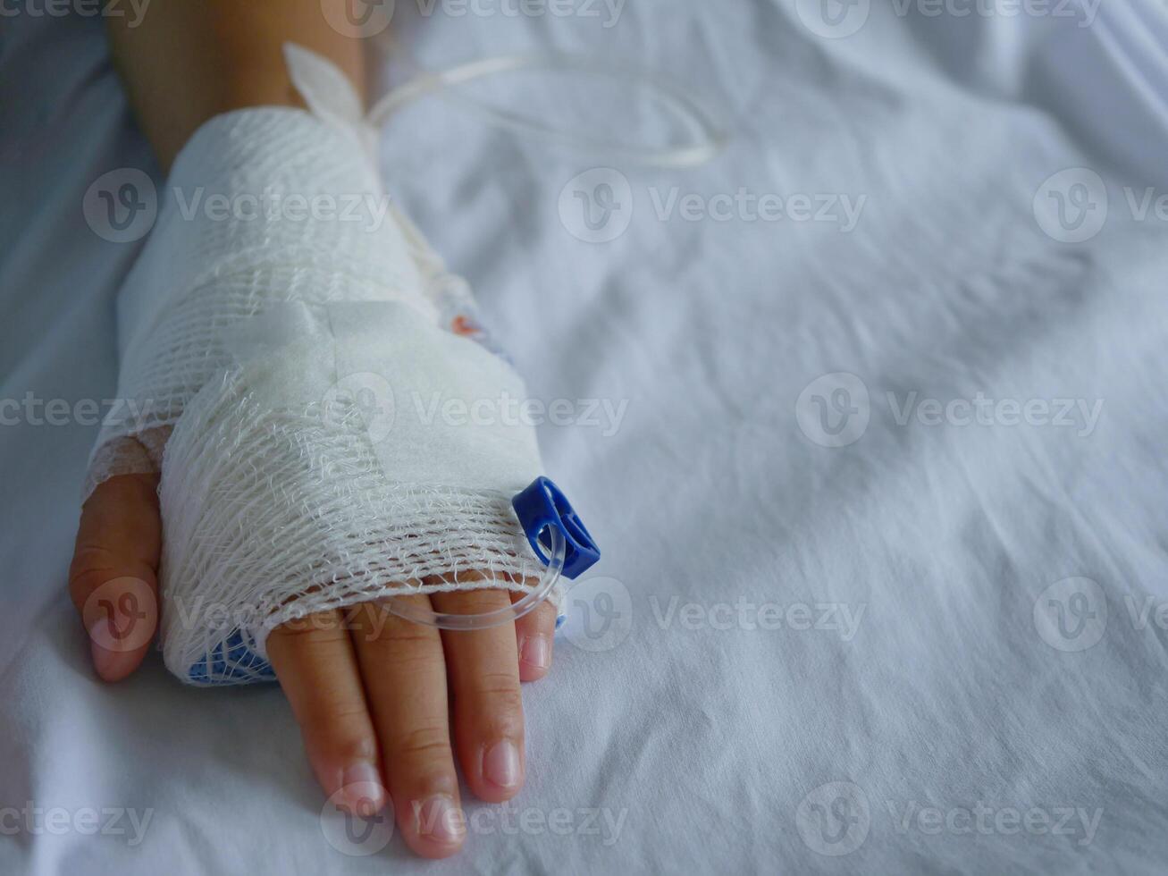 The patient's hand is wrapped in white bandages and has a saline line. photo