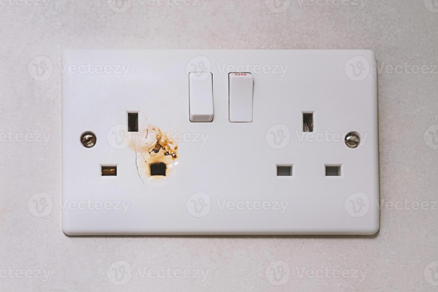 Closeup of burnt British wall outlet with melted edges. Burnt evidence of electrical meltdown, and burnt sign of potential fire risk, calling for immediate repair to ensure safer home environment photo