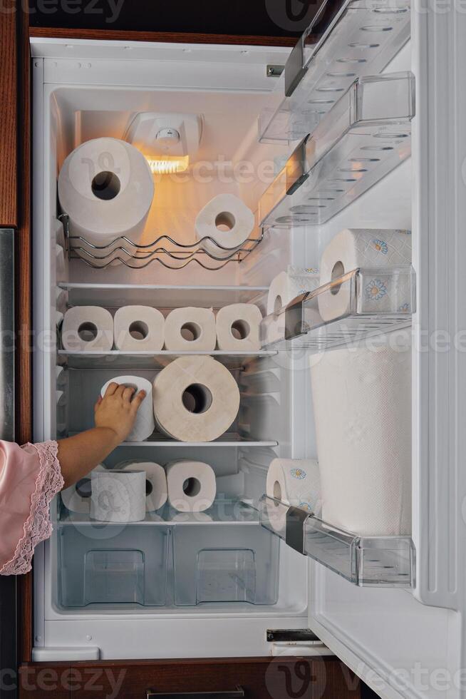 Unusual storage of toilet paper rolls inside refrigerator with hand reaching in photo