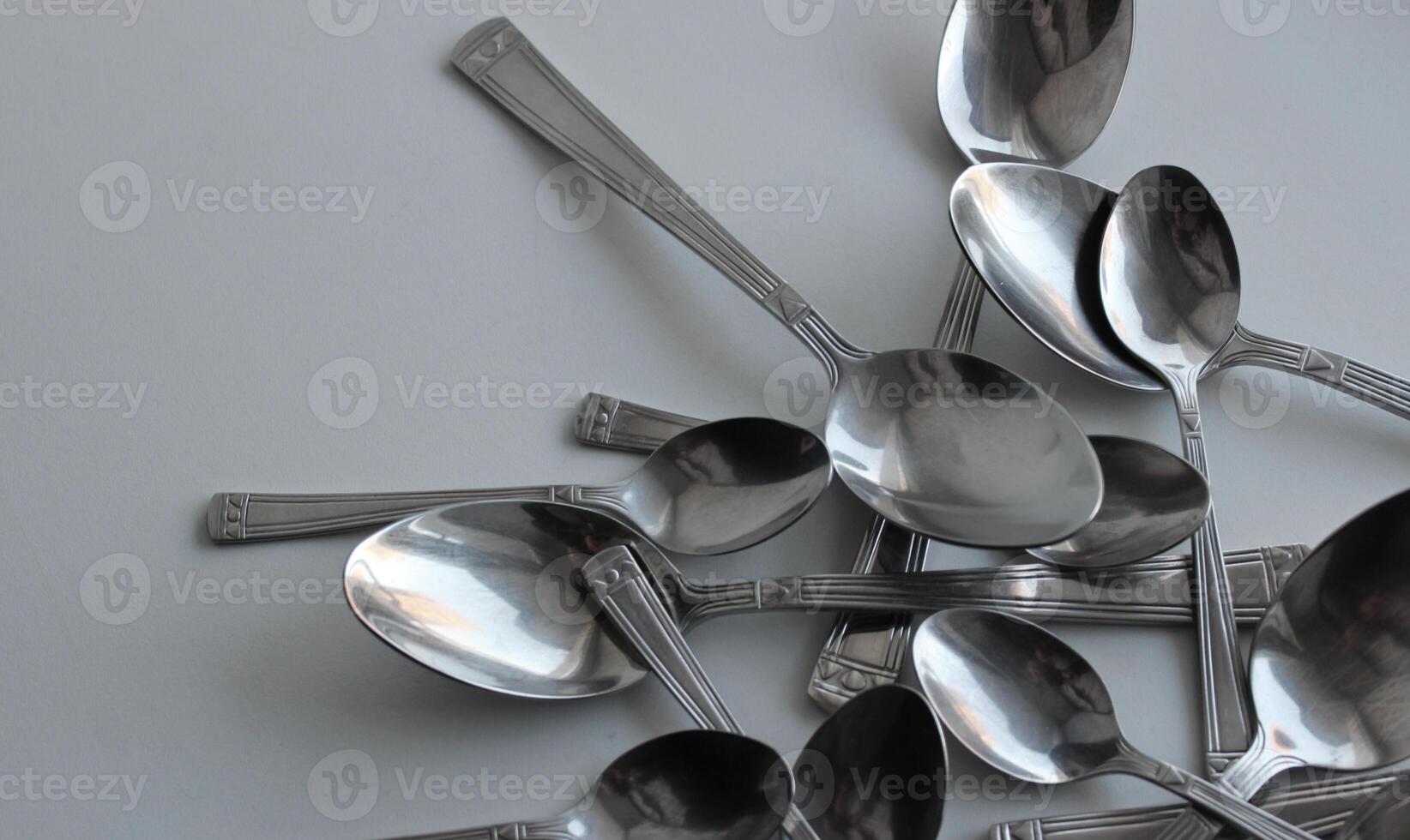Big And Small Metallic Spoons Scattered On White At A Side Of Image With Clean Part For Title Or Logo. Dishware Concept Design Stock Photo