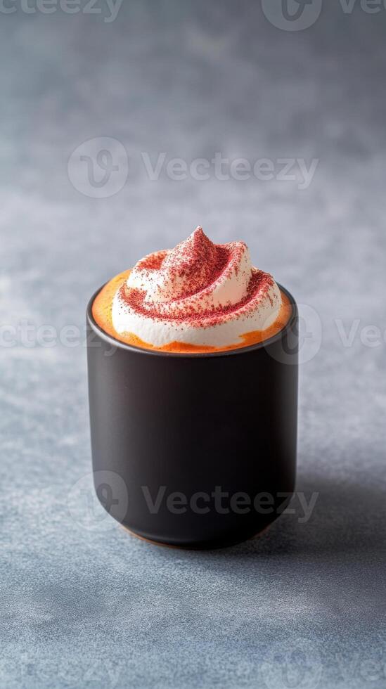 Rich turmeric-infused hot beverage topped with whipped cream sits in a black mug on a textured gray surface photo