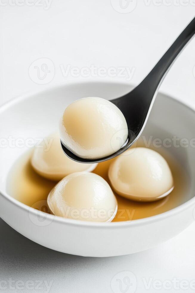 Minimalist white bowl filled with smooth glossy dumplings in light broth on a plain surface photo