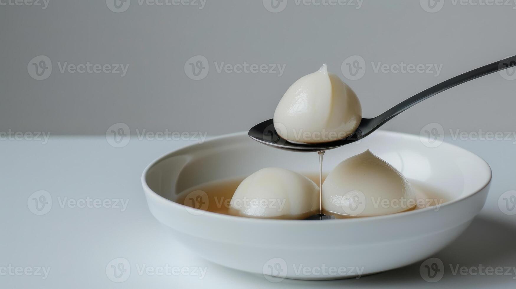 Delicate glossy dumplings in a minimalist white bowl with a spoon drizzling sauce photo