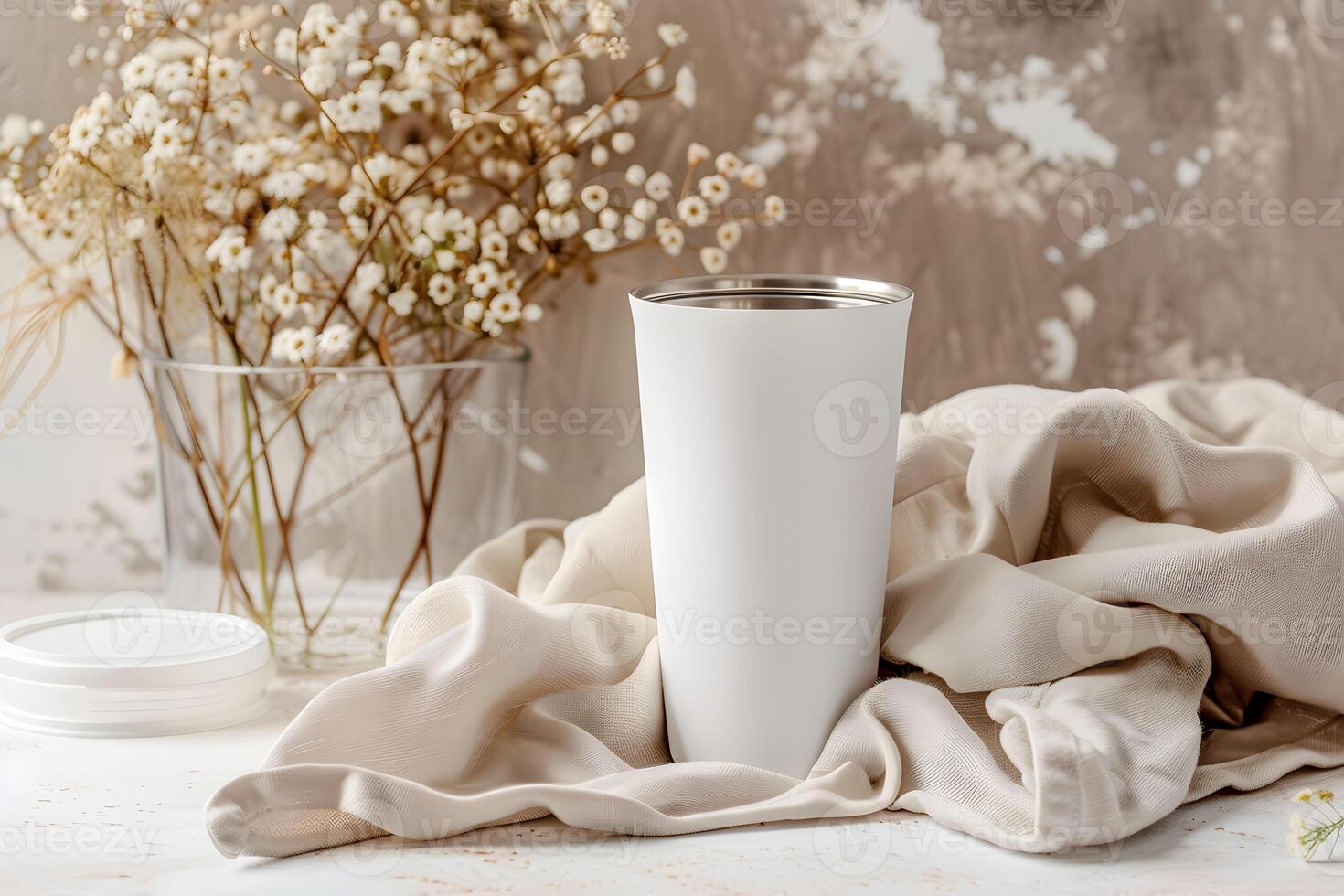 White tumbler for mockup resting on a soft fabric with delicate flowers in the background during bright daylight photo