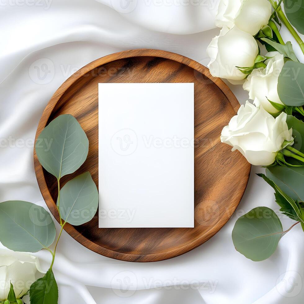 Elegant flat lay arrangement featuring a blank card for wedding invitation mockup surrounded by fresh roses and eucalyptus leaves on a wooden tray photo