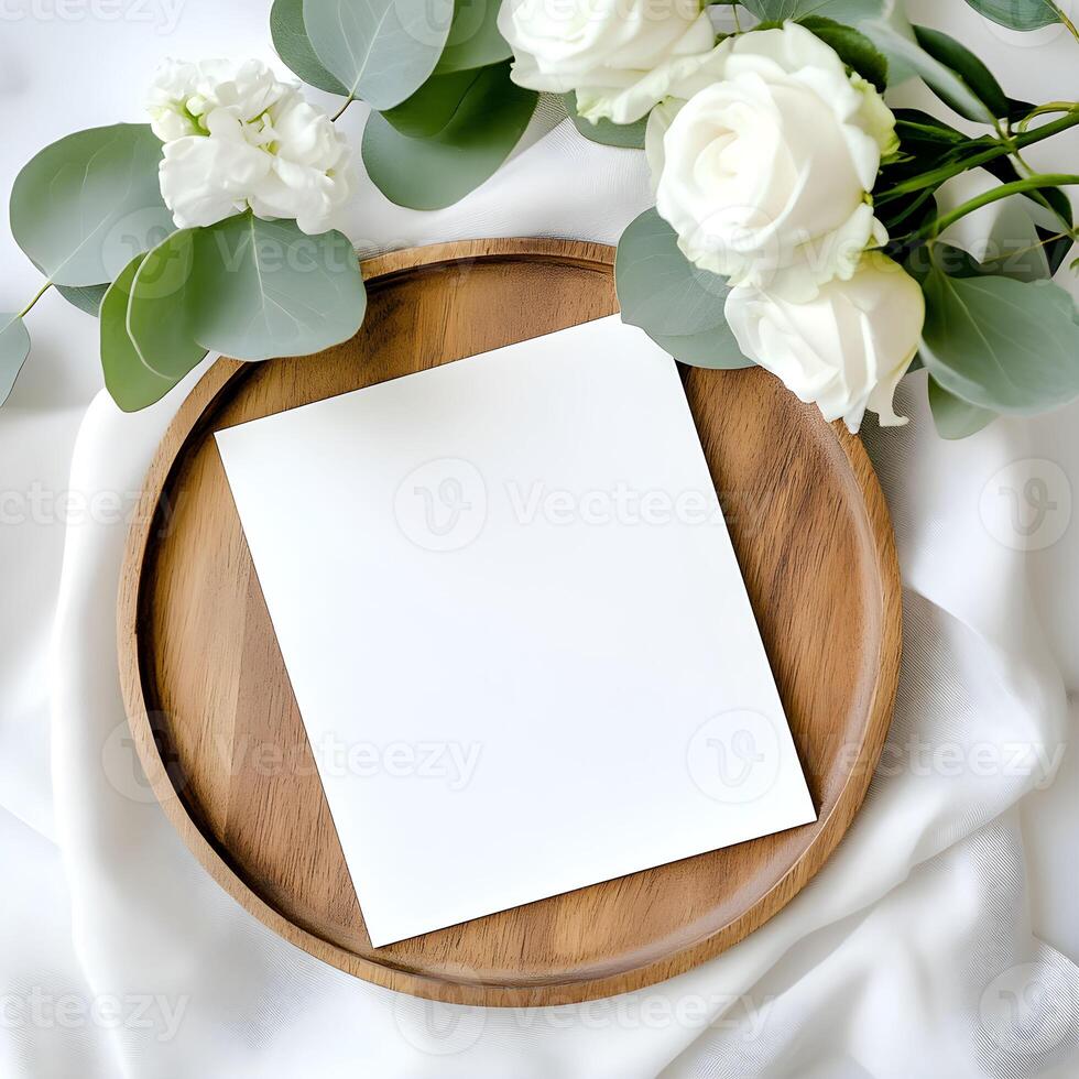 Elegant arrangement of a blank card for wedding invitation mockup and fresh white flowers on a wooden tray set against a soft white background photo