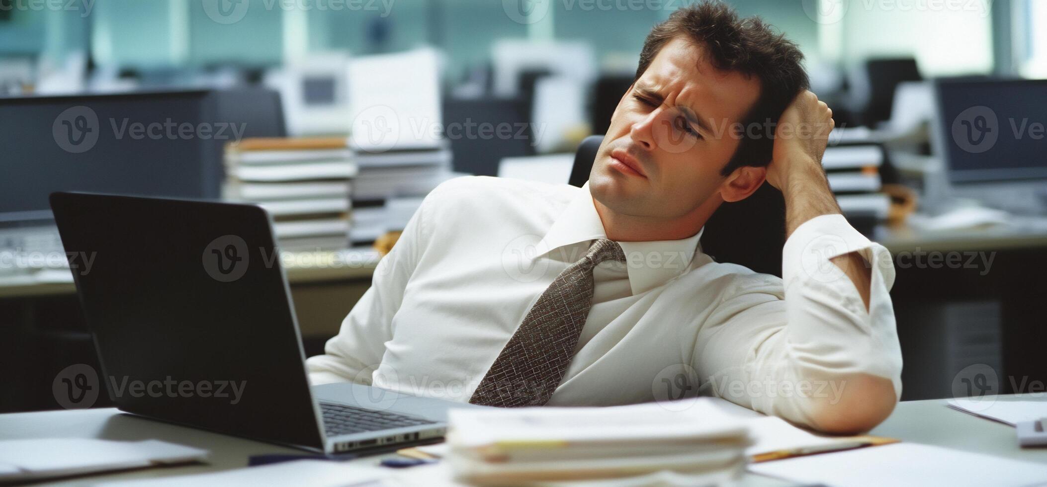 A man in a white shirt and tie is sitting on a desk with his head on his hand photo
