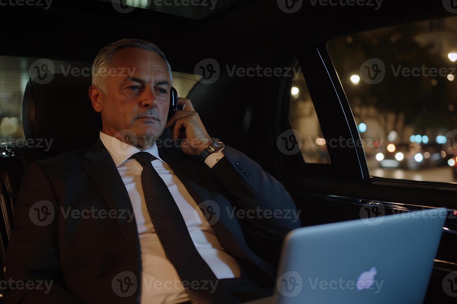 A man in a suit and tie sitting in the back seat of a car on the phone photo