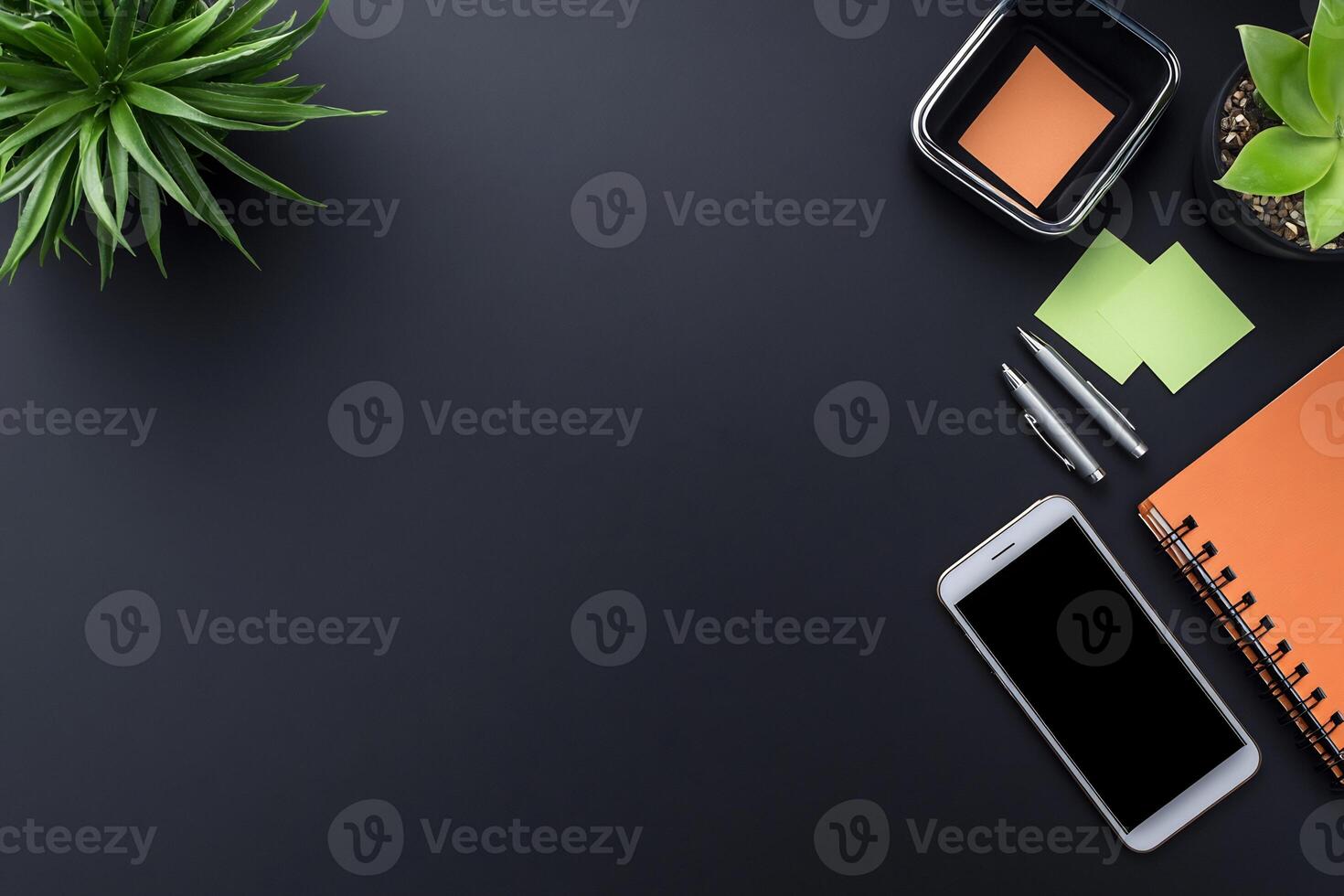 Dark gray office desk workspace with plants, sticky notes, pen, notebook, and smartphone. photo