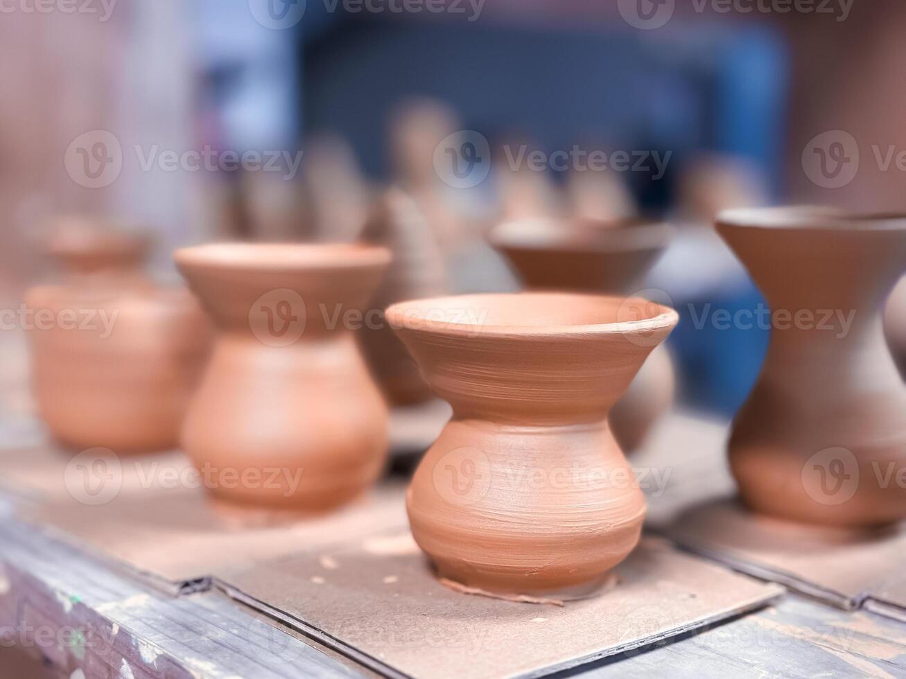 Clay pots in various shapes on a wooden table at pottery workshop photo