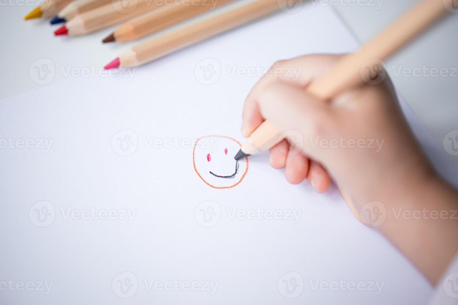Child drawing smiley face with colored pencils on white paper photo