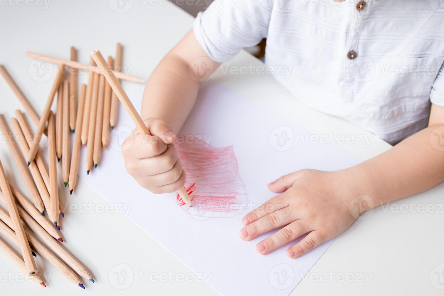 Child drawing with colored pencils on white paper photo