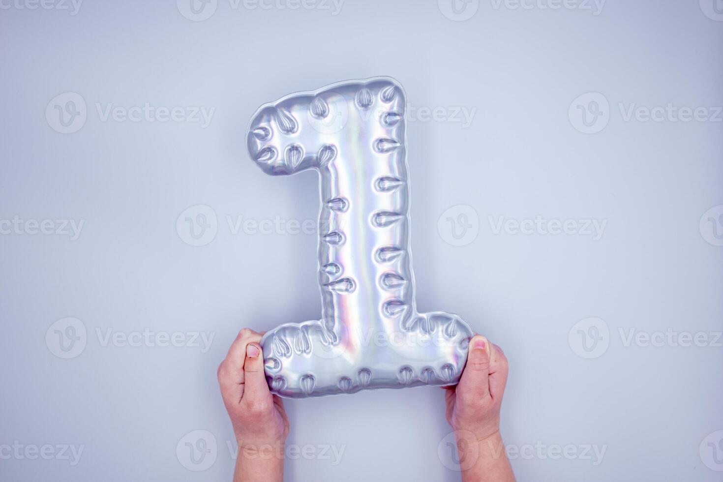 Child holding silver number one balloon on light background photo