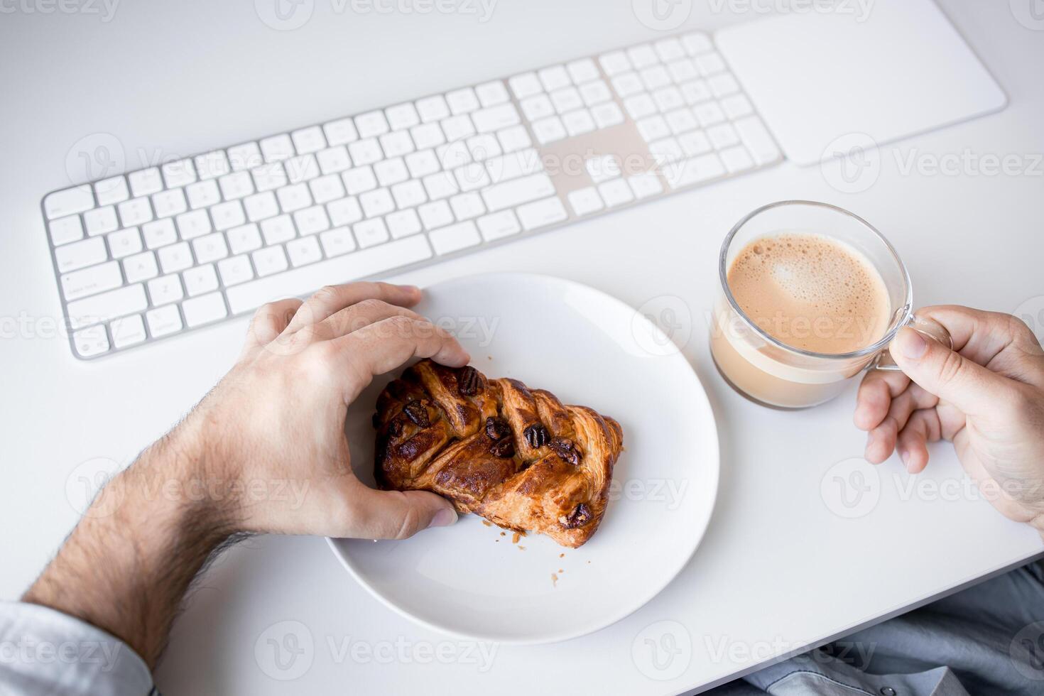 Caucasian male adult enjoying coffee and pastry at office desk with keyboard photo