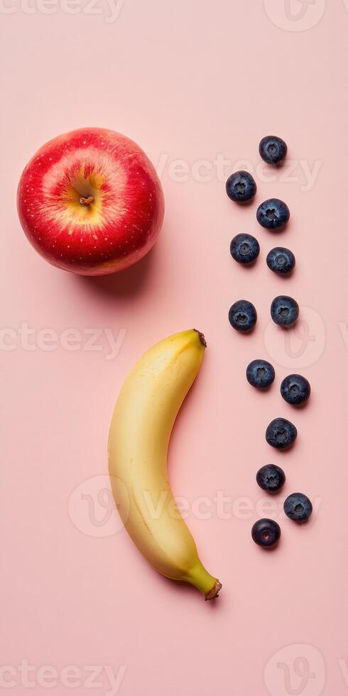 Minimalistic flat lay with bright red apple, banana, and blueberries on pink background for modern design photo