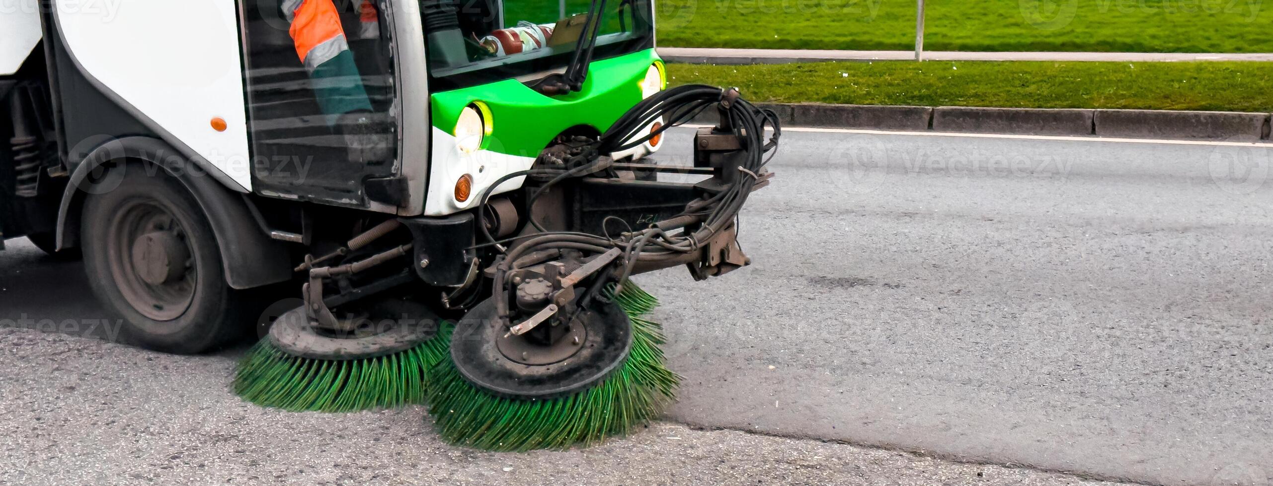 Street sweeping vehicle cleans urban road with rotating brushes photo