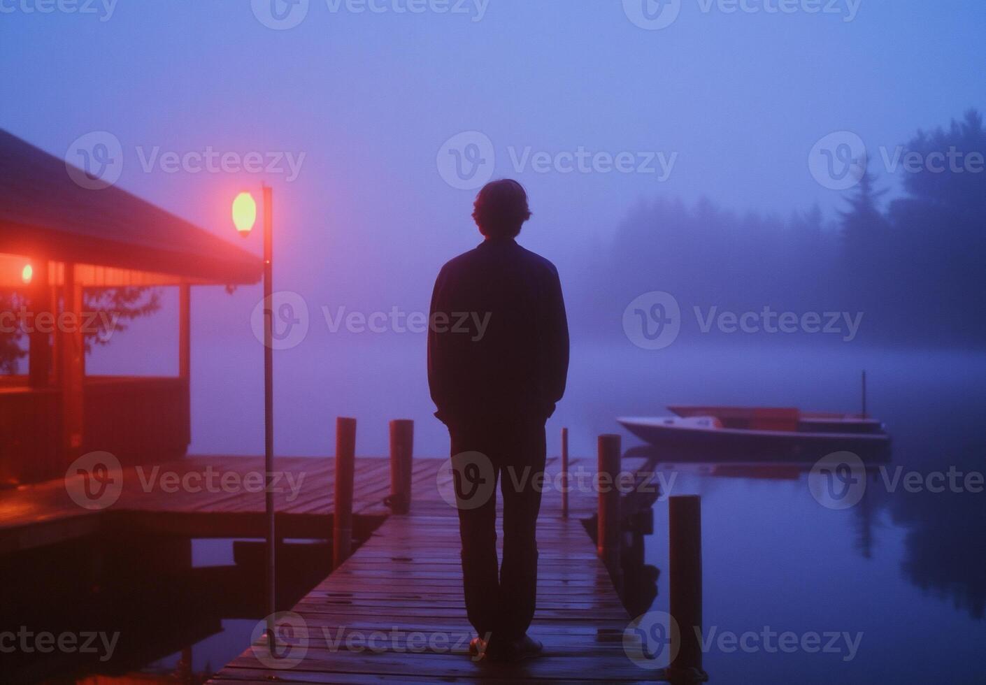A person stands on a foggy dock, illuminated by soft lights. photo