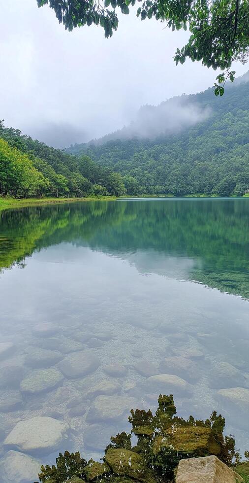 Serene Mountain Lake With Crystal Clear Water And Lush Green Forest Reflections Under Foggy Sky photo