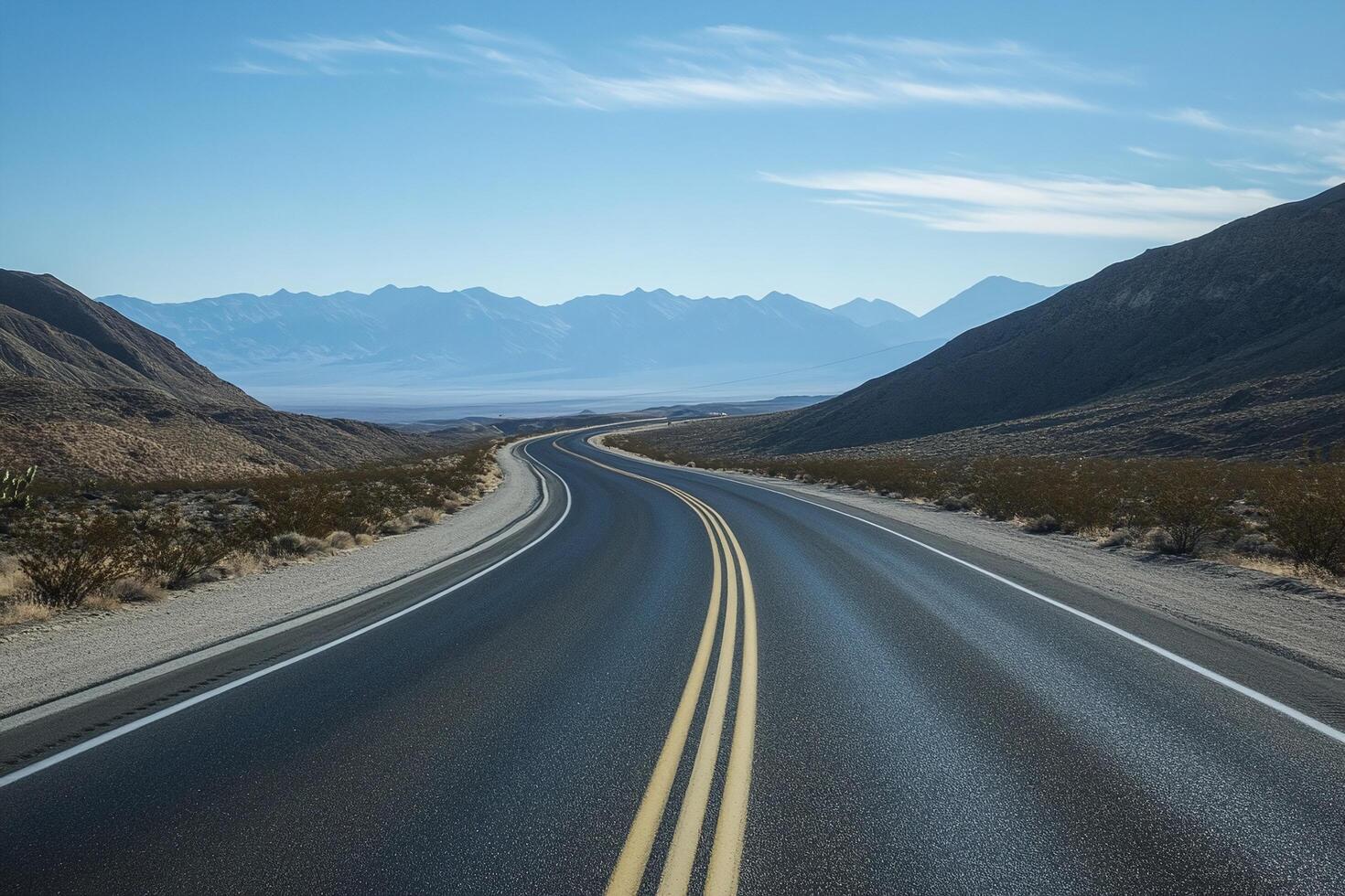 Winding Asphalt Road Through Desert Hills Leading Towards Distant Blue Mountains and Clear Sky photo