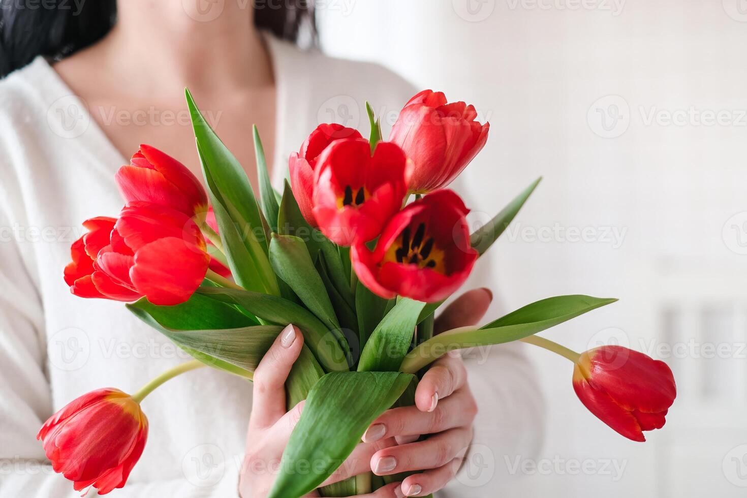 Close-up of a woman in a white sweater with a bouquet of red tulips photo
