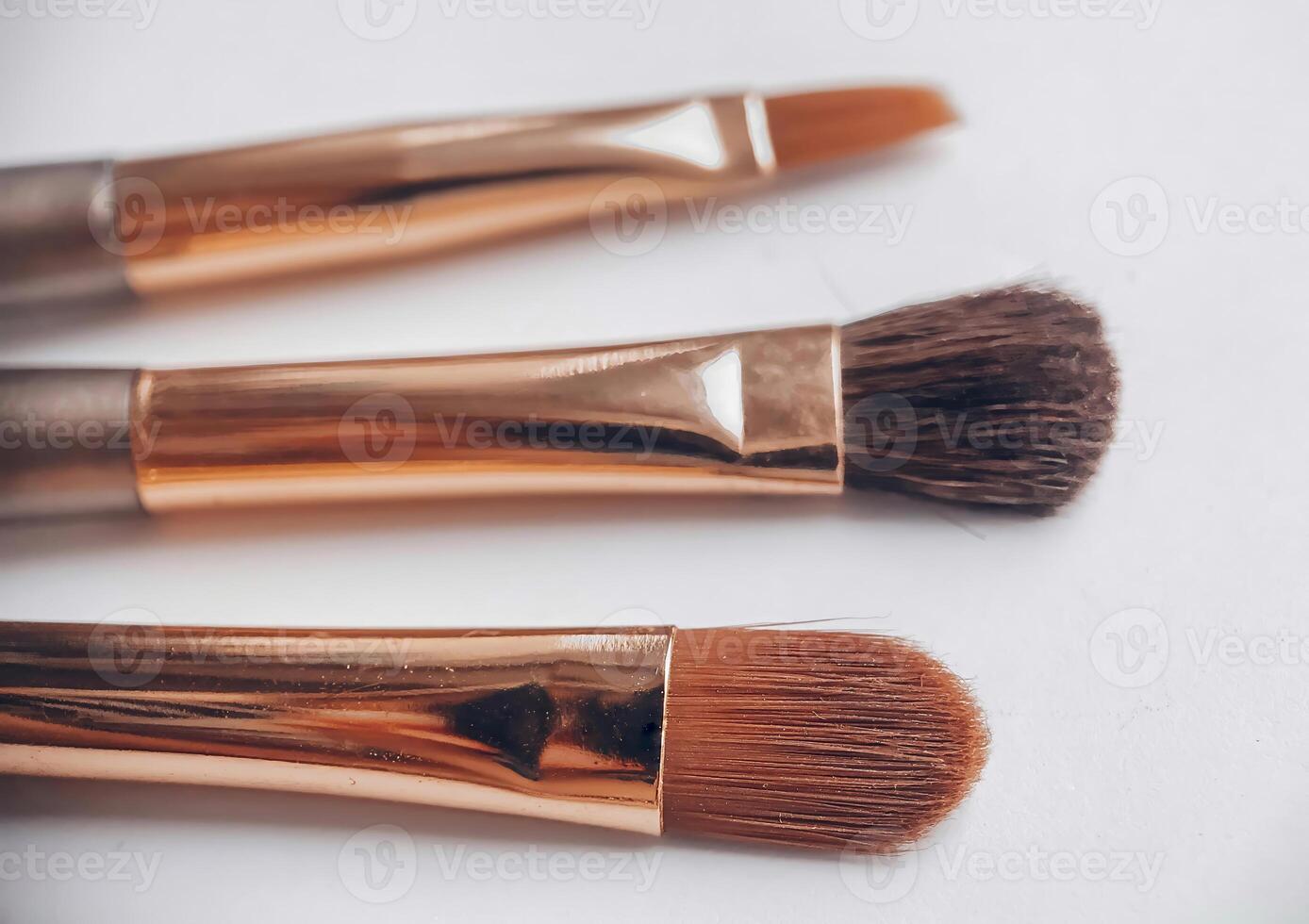 Close-up of three makeup brushes with golden handles on a white background photo