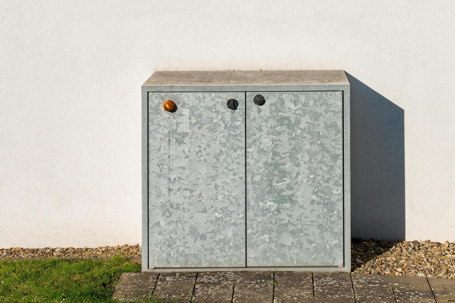 Modern metal storage cabinet placed against a white wall outdoors photo