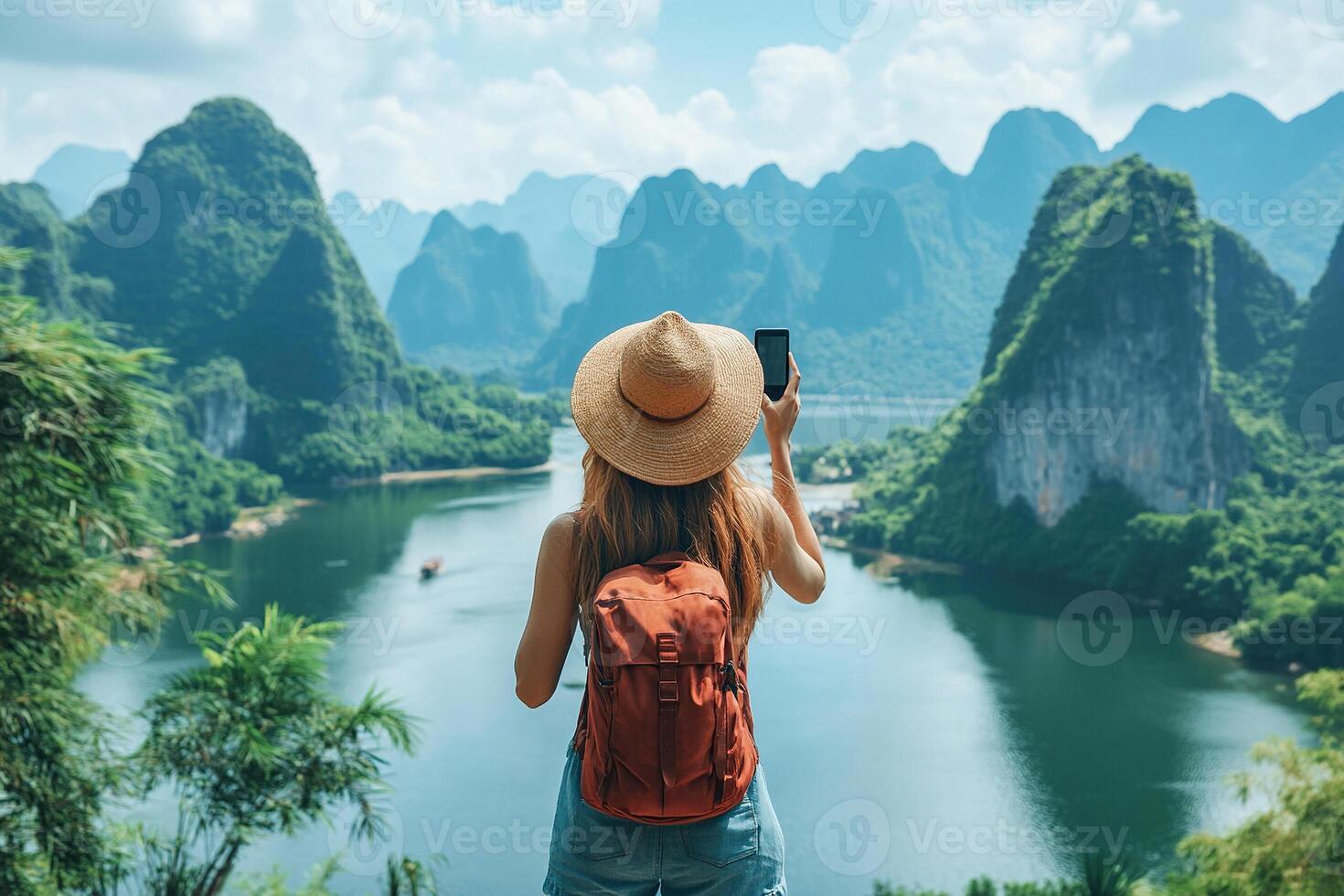 A female traveler in a hat with a backpack on her back takes a photo of an amazing landscape with rocks, sea and blue sky on her smartphone during her vacation. A female tourist during her vacation.