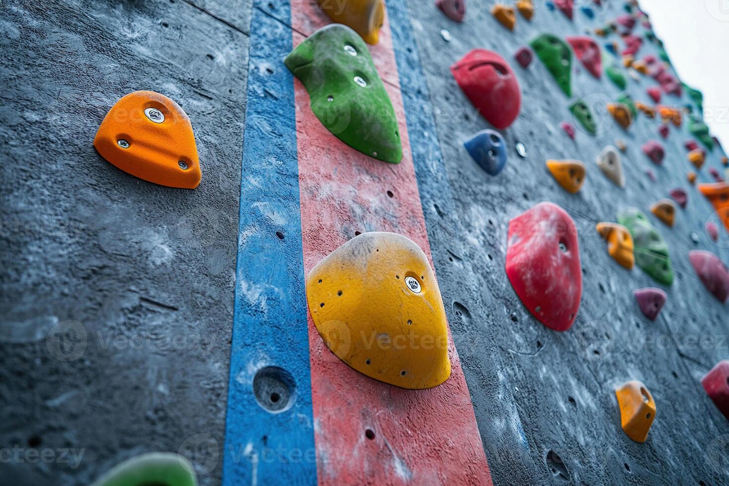 Close-up of climbing wall grips and handles of different shapes and sizes on a grey indoor climbing wall. The grips on the climbing wall are of different colors. photo