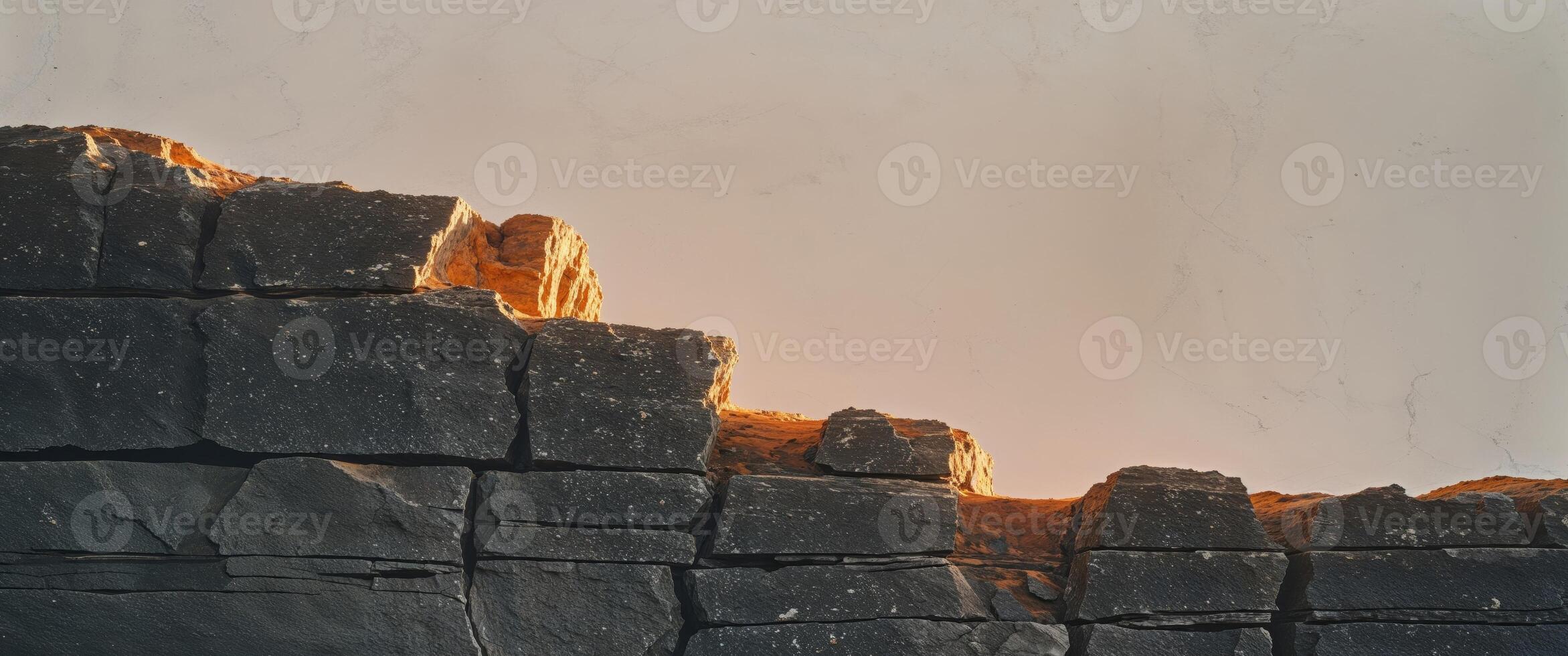 A sunset over a wall of black rocks photo