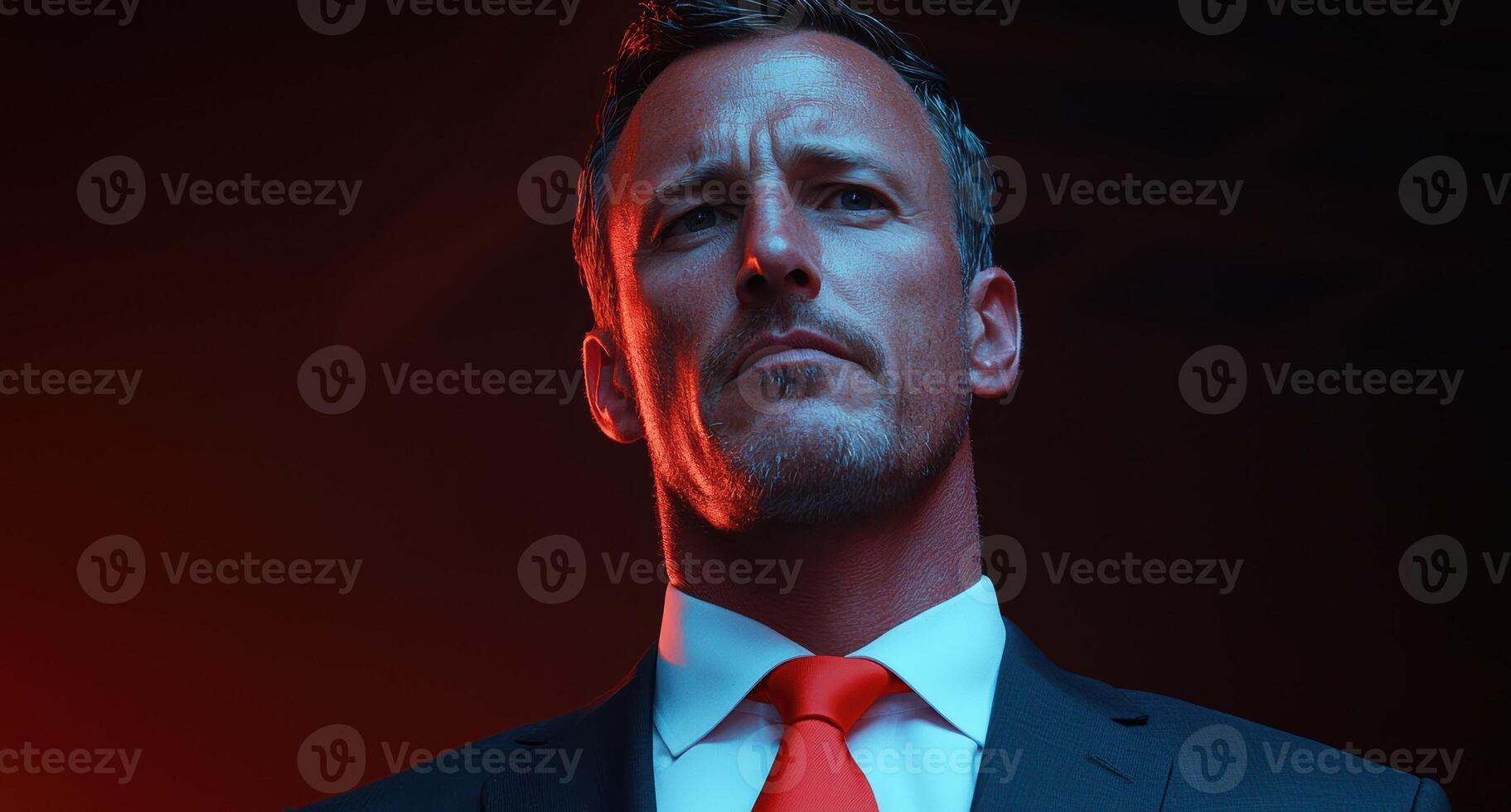 A serious man in a suit with a red tie looks up photo