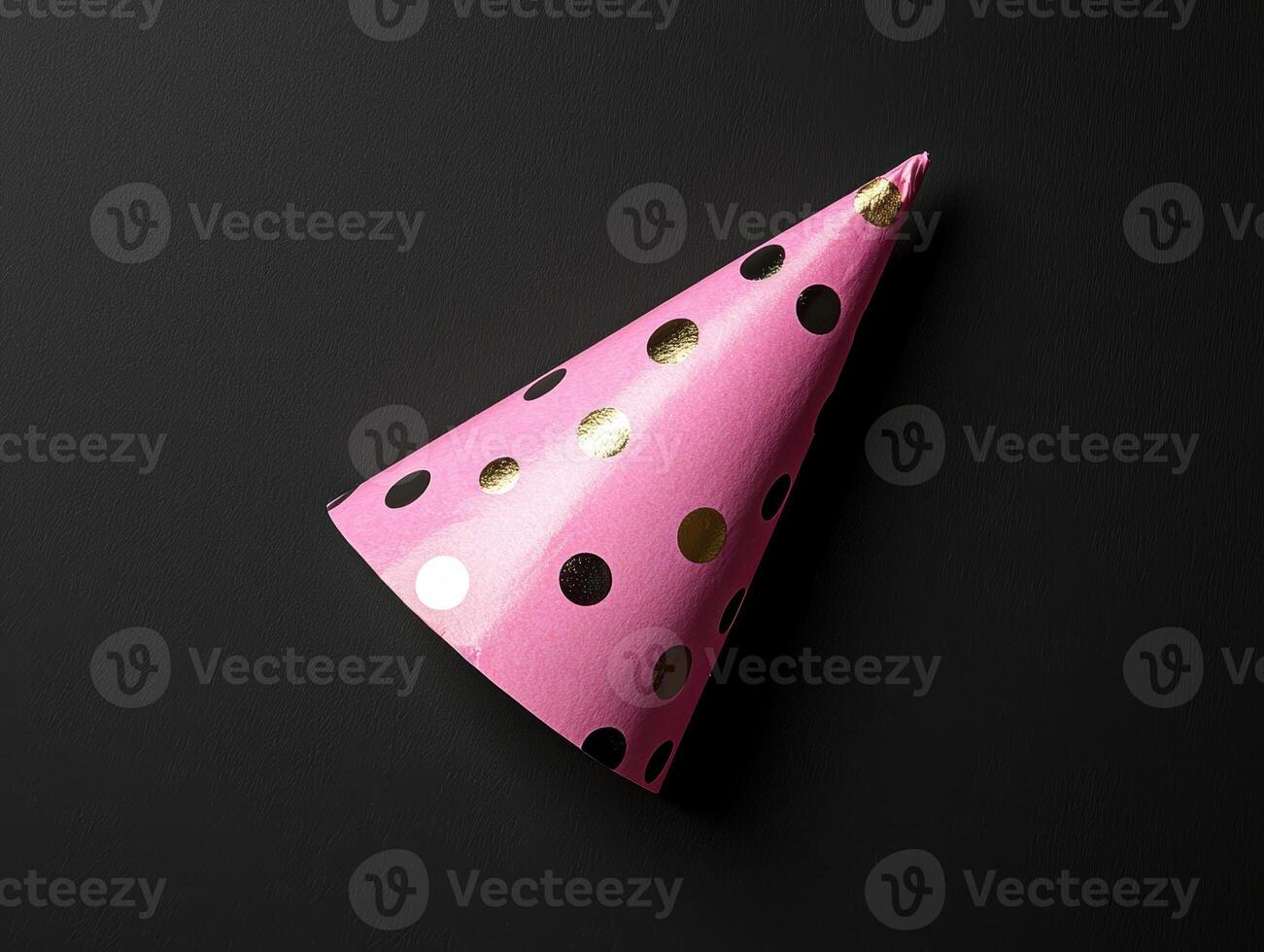 Pink party hat with gold and black polka dots on a dark background photo