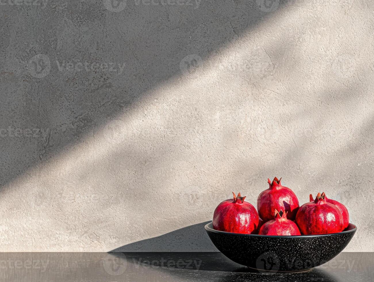Pomegranates in a bowl with light and shadows on a textured wall photo