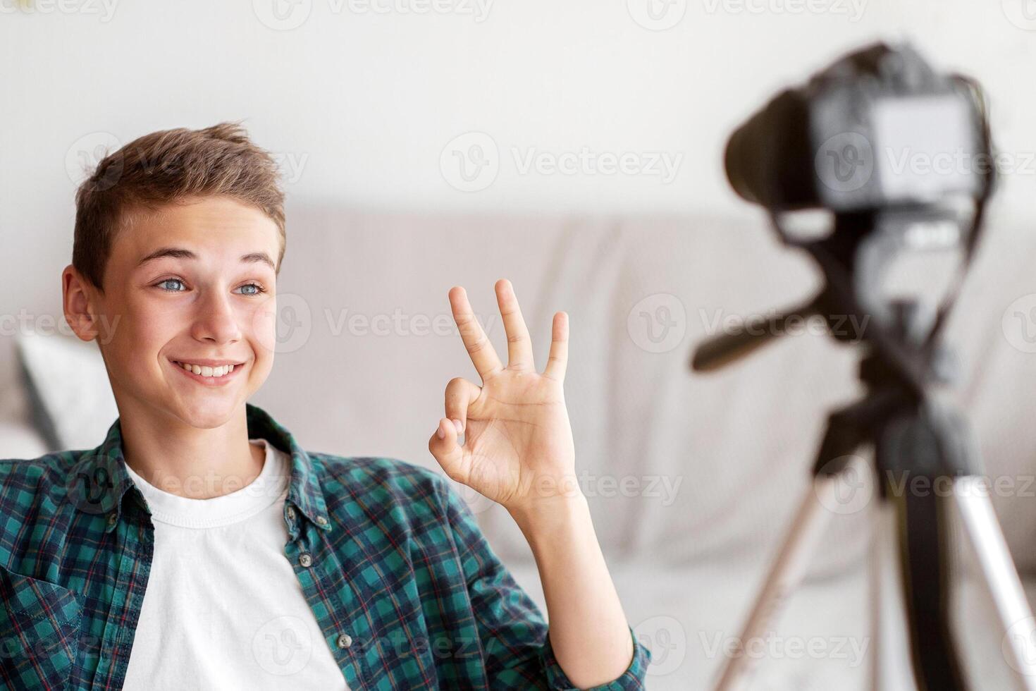 Positive teen boy broadcasting from home, showing okay gesture at camera photo