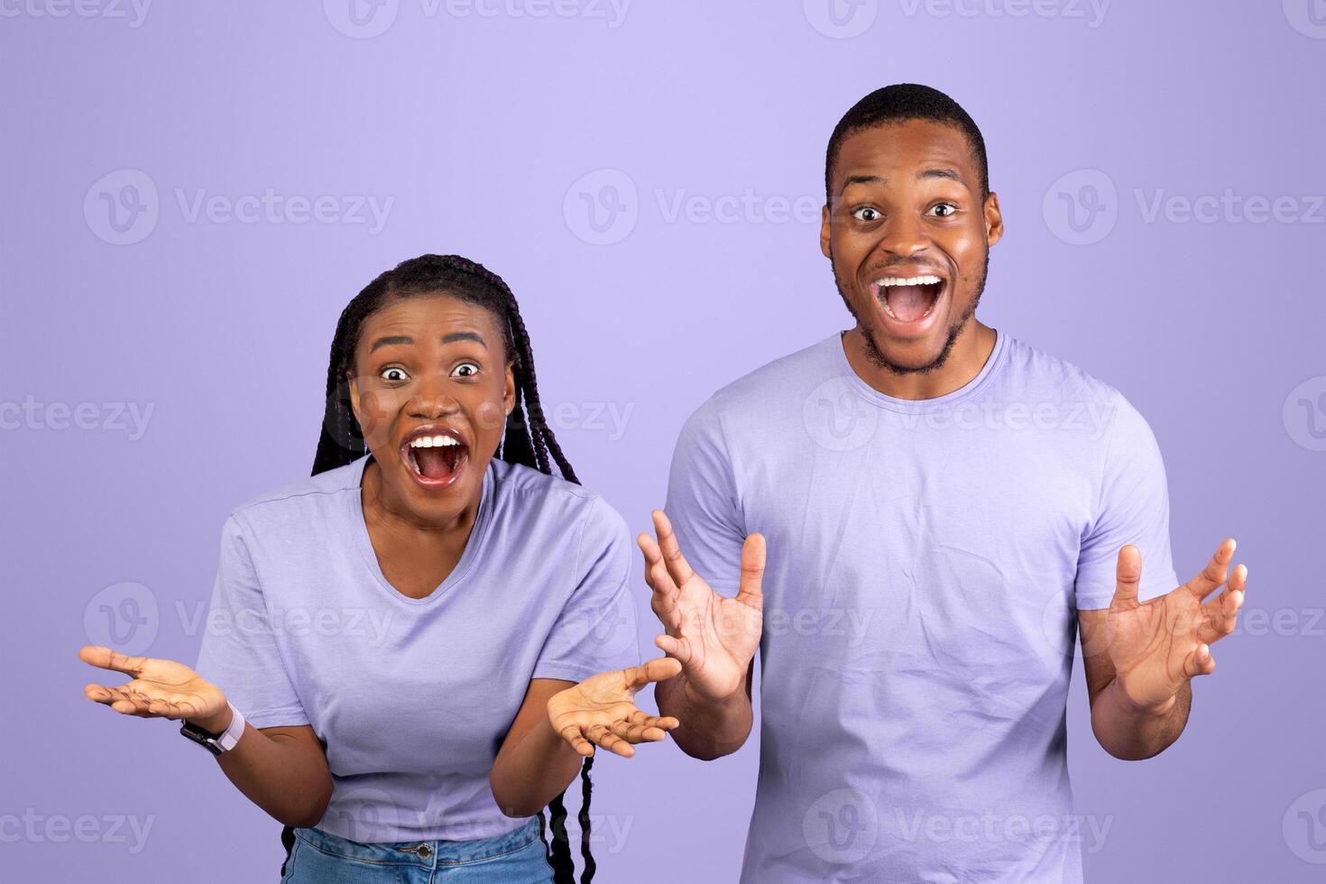 Omg. Portrait of excited young black man and woman with open mouth spreading hands and looking at camera. Emotional happy African American couple posing isolated over violet studio background photo