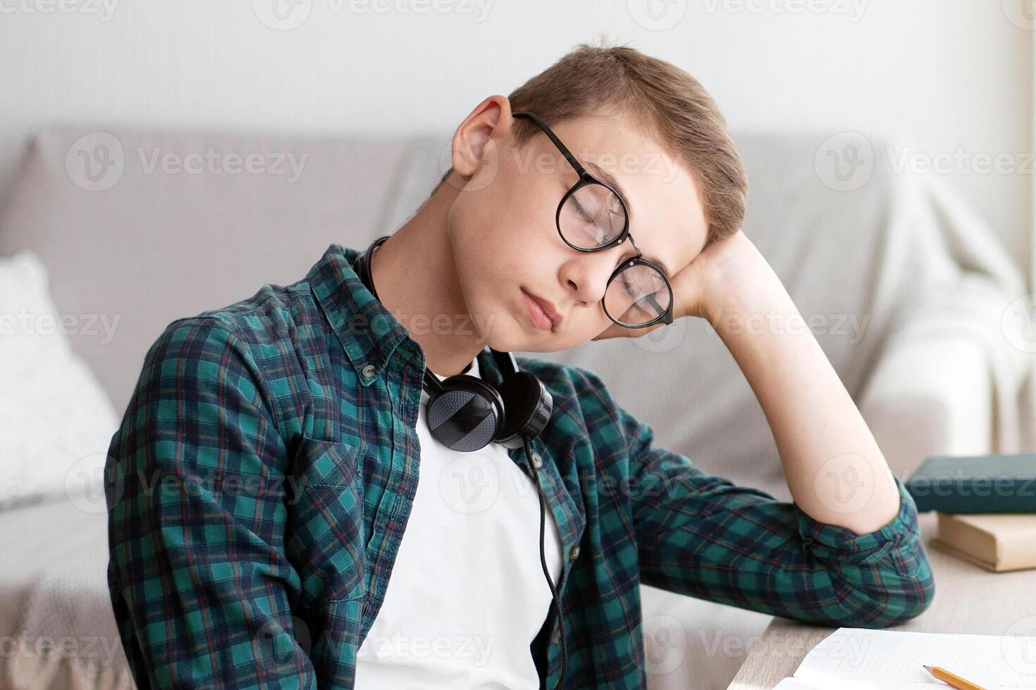 Teenager having nap while studying at home, sitting at desk, empty space photo