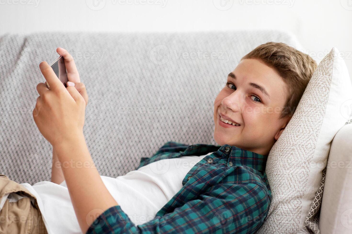 Side view of positive teen guy gaming on smartphone while resting at home photo