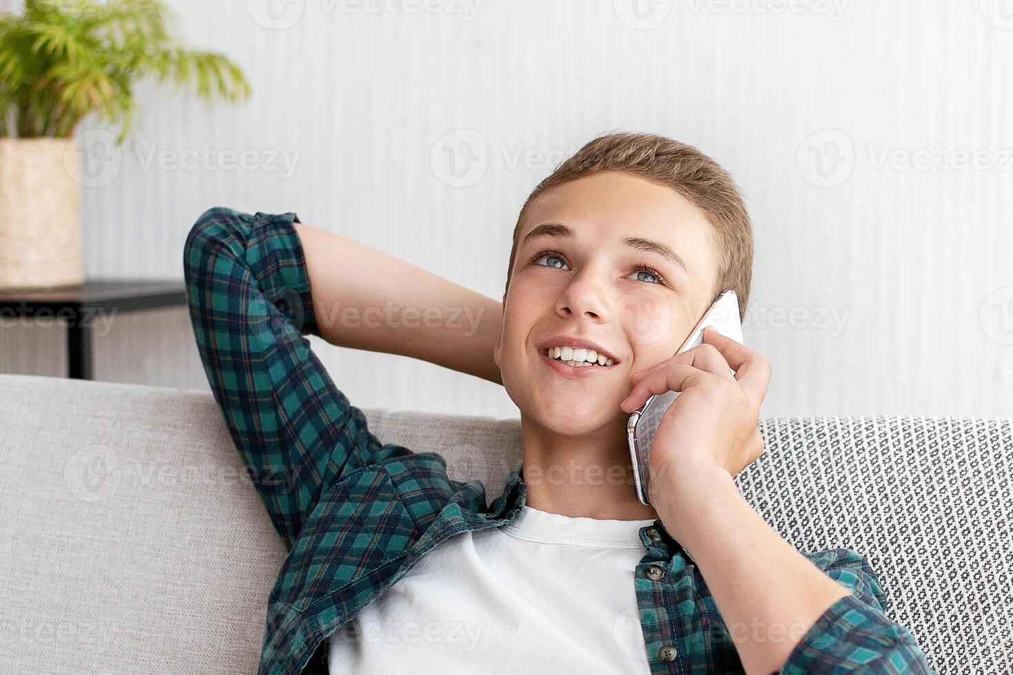 Carefree teen guy talking on mobile phone with friends, sitting at home alone, empty space photo