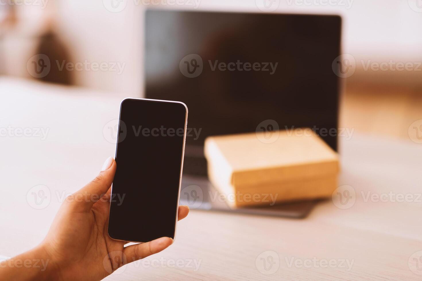 Technology Concept. Unrecognizable black woman holding and showing smartphone with blank empty screen for mock up. Laptop computer with present box or delivery package on keyboard in the background photo