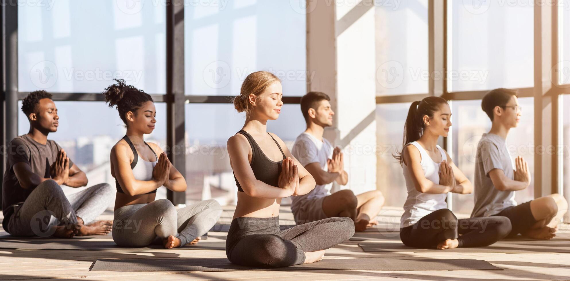 Meditation Session. Group Of Diverse Sporty People Practicing Yoga In Modern Gym, Sitting In Lotus Position With Namaste Gesture, Side View photo