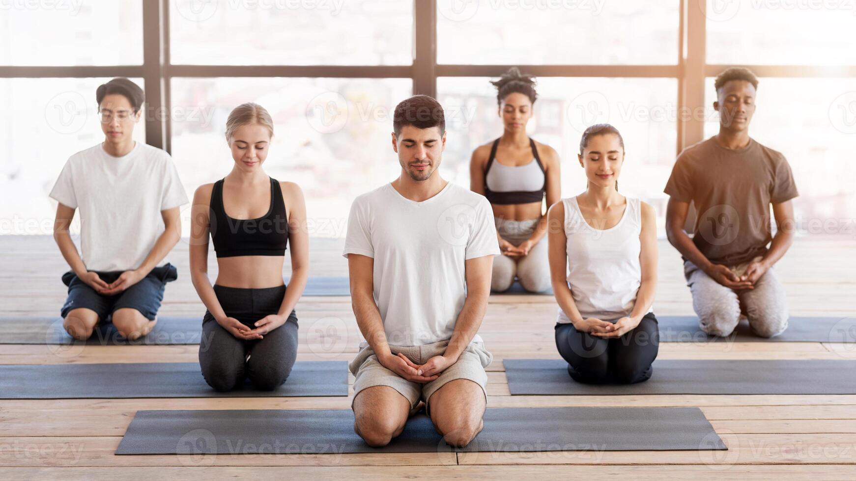 Group Meditation. Young People Practicing Breathing Yoga Exercises With Instructor In Modern Studio photo