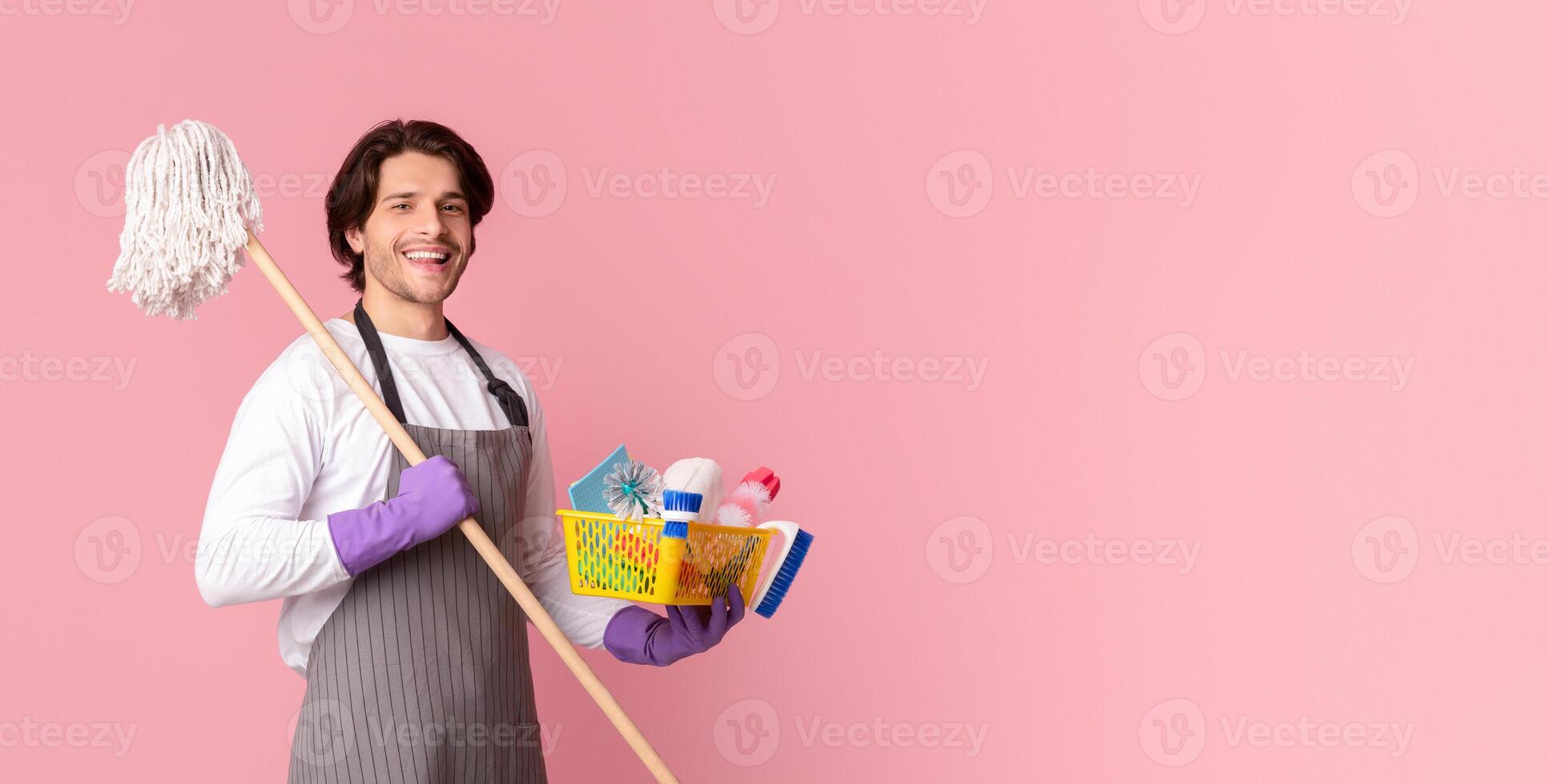 Spring-Clean Service Worker. Portrait Of Happy Man Holding Mop And Bucket With Cleaning Tools, Standing Over Pink Studio Background, Free Space photo