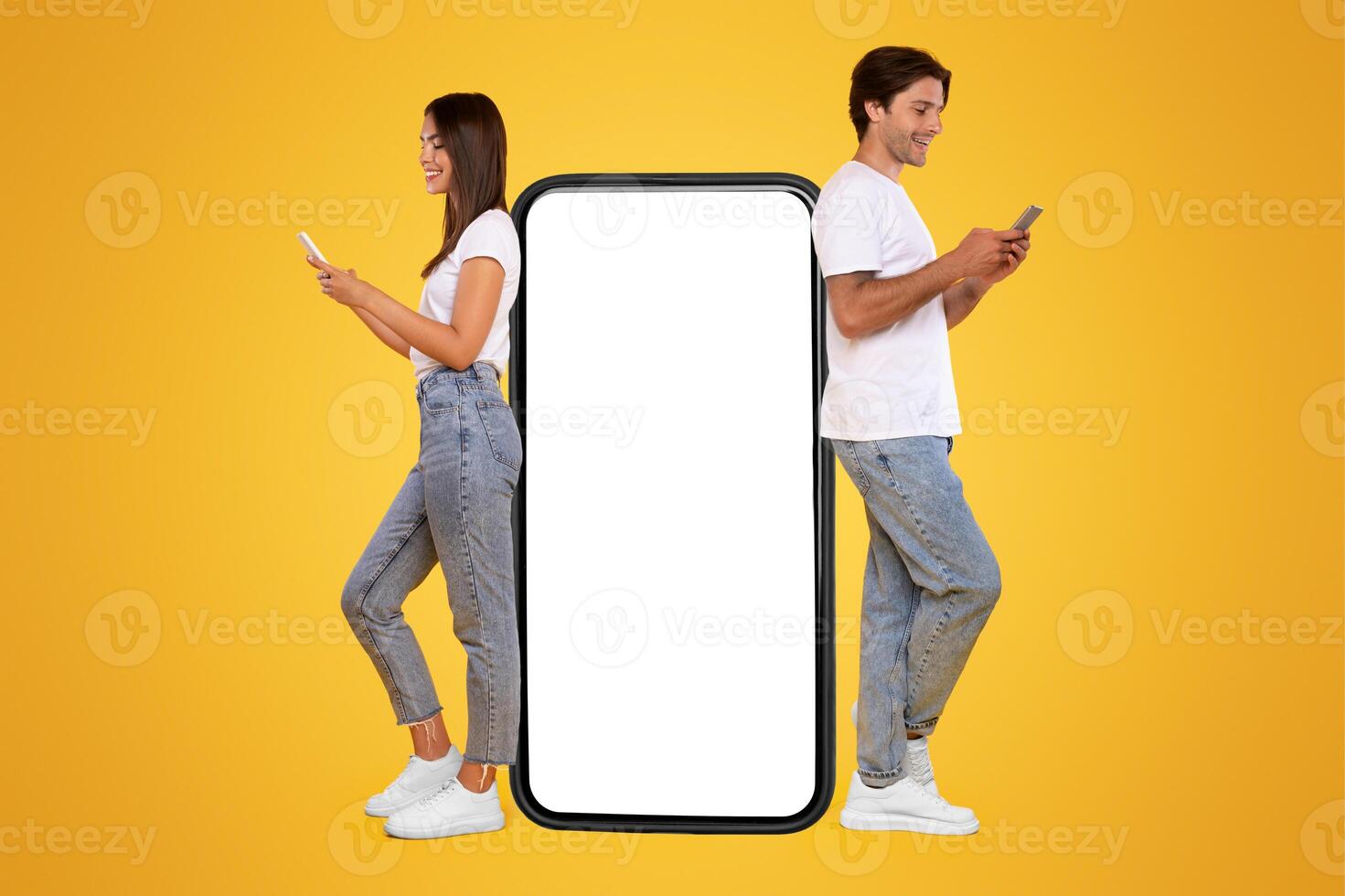 Great App. Excited Couple Leaning On Big Smartphone With Blank White Screen Using Cell Phones, Cheerful Guy And Lady Chatting On Social Media, Standing On Yellow Orange Background, Mock Up, Full Body photo