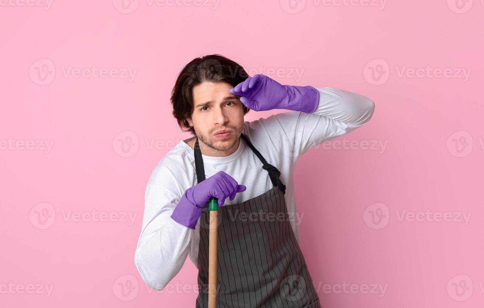 Young Man Tired After Cleaning, Leaning At Mop Handle, Exhausted After Tidying Up Apartment, Standing Over Pink Background With Free Space photo
