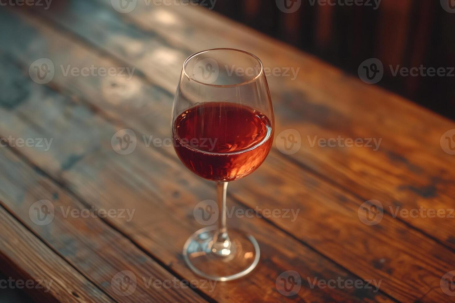 Glass of wine standing on wooden table in warm light photo