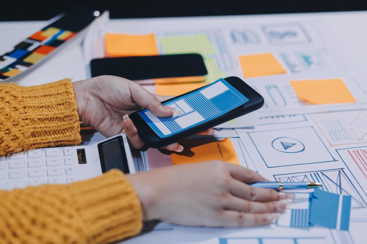A person is using a smartphone on a table with a paper and pencils photo