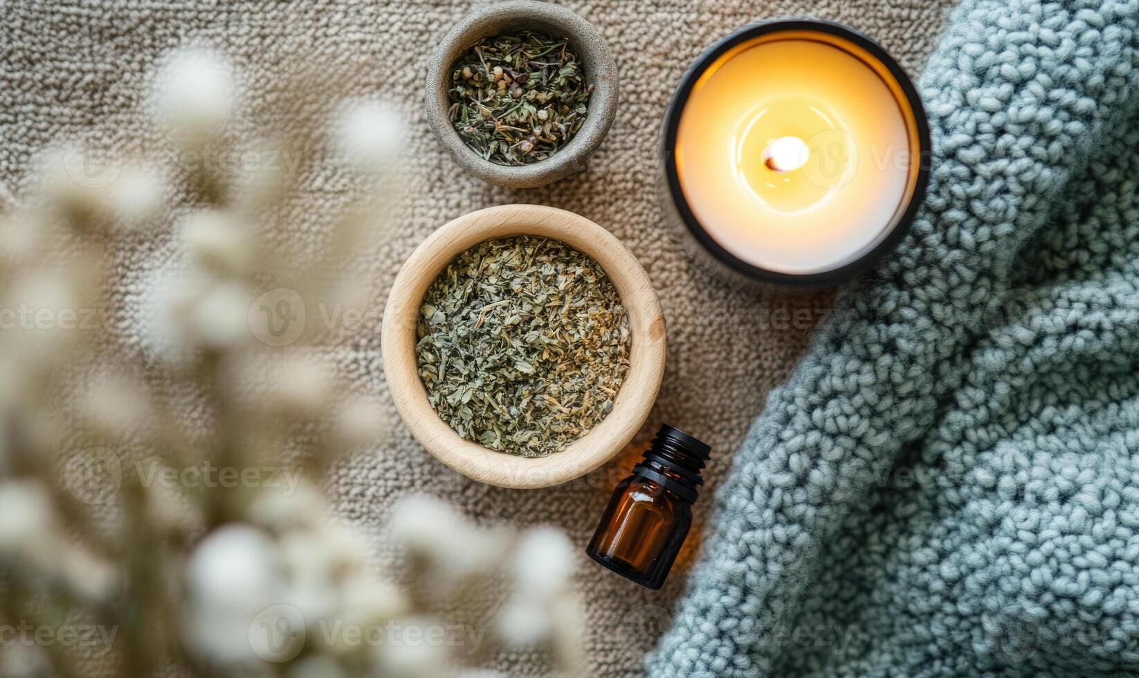 A candle is lit next to a bowl of herbs and a bottle of essential oil photo